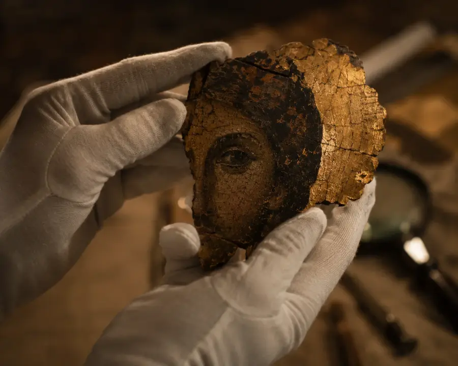 Gloved hands examining a damaged painted fragment in Luna's restoration studio
